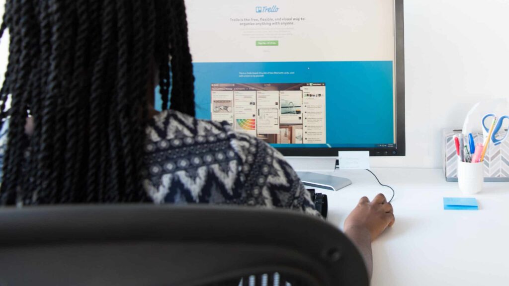 Mulher negra de costas, utilizando o Trello no computador
