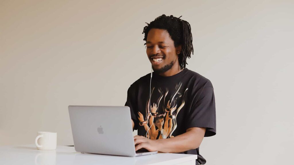 Homem negro sorrindo olhando para o computador, em uma entrevista de emprego online