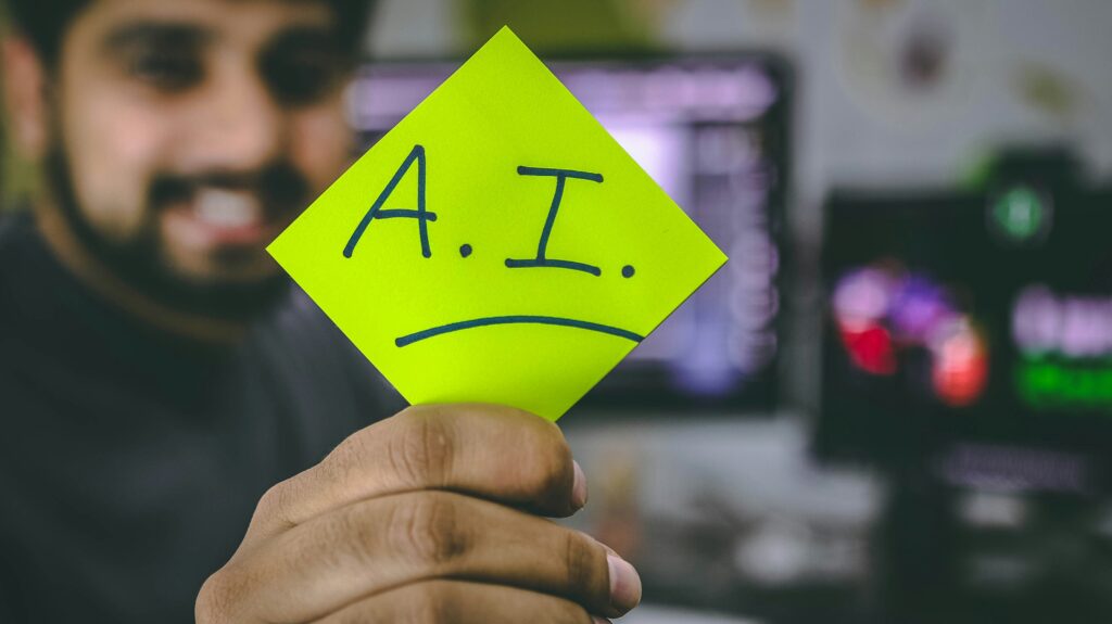 Uma pessoa segurando um post-it verde brilhante com o texto escrito à mão A.I. O fundo está desfocado, mostrando telas de computador e uma mesa, enfatizando um ambiente relacionado à tecnologia.