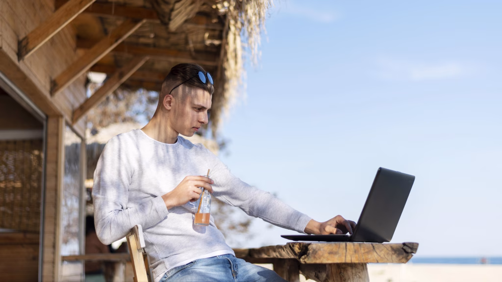 Pessoa trabalha remotamente ao ar livre, com um copo de suco na mão.