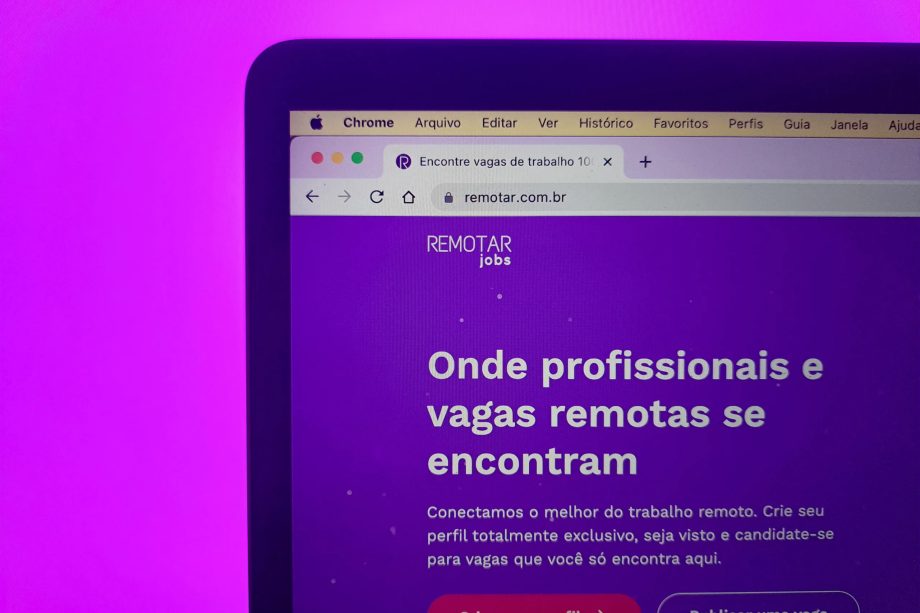 Uma tela de computador exibe um site com o título Remotar jobs e texto em português sobre conectar profissionais com oportunidades de trabalho remoto. A tela está contra um fundo roxo.