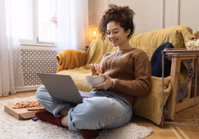 Mulher está sentada no chão, com um laptop no colo. Imagem para destacar o artigo sobre Vagas remotas abertas.