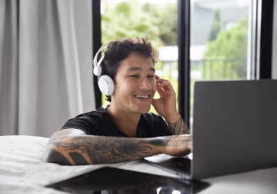 Confira vagas remotas em administração e finanças. A foto apresenta jovem com fone de ouvido e laptop, trabalhando remotamente